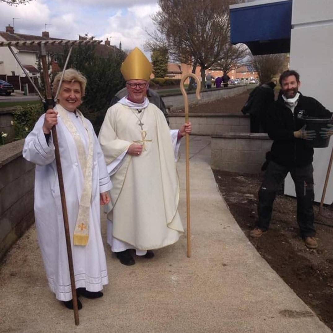 A priest and bishop with a gardener blessing a new wildflower meadow.