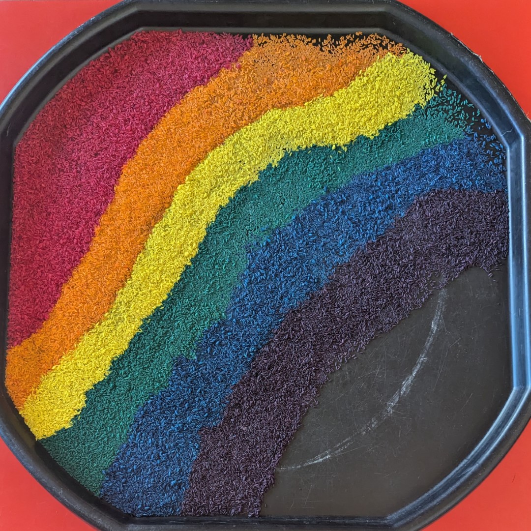 Rainbow coloured rice in layers to represent a rainbow on a large black plastic sheet on a red background